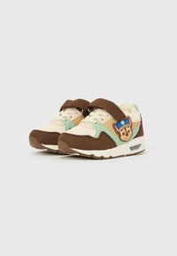 Baskets avec une palette de couleurs marron, crème et menthe; matériaux en toile et daim; dotées d'un badge de personnage et d'une bride en Velcro.