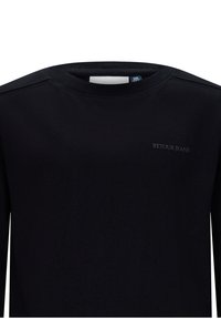 Maglietta nera a maniche lunghe realizzata in un tessuto morbido, con scollatura a girocollo e un sottile logo "RETOUR JEANS" stampato sul petto.