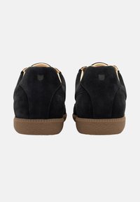 Schwarze Wildledersneaker mit einer braunen Gummisohle, die ein tiefes Design und minimalistische Details an der Ferse aufweisen.