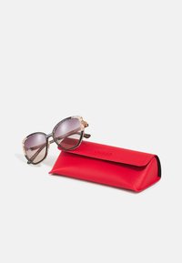 Black sunglasses with gradient lenses, decorated with glittery gold accents on the frame. Red leather case with "GUESS" embossed on it.