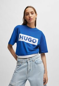 Blå bomull T-skjorte med en stor hvit "HUGO" logo over brystet, kombinert med lyse myke-jeans med en avslappet passform.