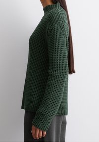 Zielony, teksturowany sweter dziany z wysokim kołnierzem i długimi rękawami. Projekt ma luźny krój i ściągacze na mankietach.