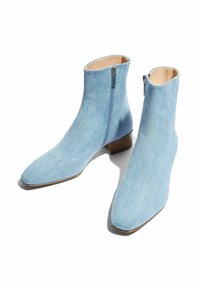 Botines de ante azul claro, fabricados en una tela de denim con una textura suave, puntera puntiaguda y cremallera lateral. Presentan un bajo tacón de madera.