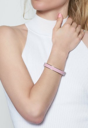 Pink enamel bangle bracelet with silver metal accents, worn on a bare arm against a white ribbed top. Smooth surface, minimalist design.