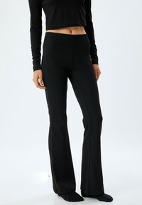 Pantalones negros acampanados hechos de una tela elástica con una cinturilla ancha. Presentan una textura suave y costuras laterales ajustadas para un aspecto entallado.
