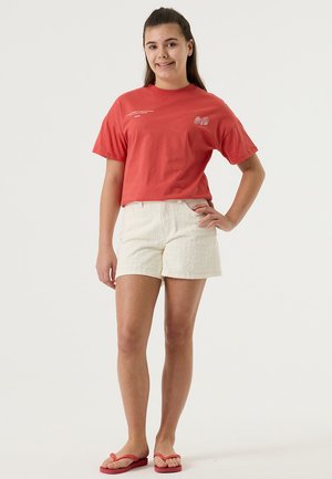 Rode katoenen T-shirt met korte mouwen en wit geborduurde tekst, gecombineerd met wit gestructureerd korte broekje en rode teenslippers.