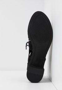 Czarne zamszowe buty z teksturowaną gumową podeszwą z poziomymi rowkami, zaprojektowane z otwartymi wycięciami i sznurowadłami po bokach.