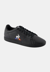 Des baskets noires avec une tige en cuir lisse, présentant un logo et des accents de couleur orange et bleu. Design classique à lacets, profil bas.