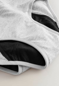 Pelēkas un melnas sporta krūšturis ar gludu tekstūru, izsistām detaļām, kontrastējošu odere un izšuvumiem. Materiāls izskatās elastīgs un elpojošs.