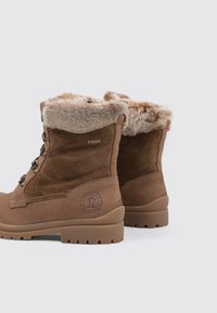 Botas impermeables marrones de ante con un collar de pelo sintético, que cuentan con ojales de metal, una suela de goma texturizada y un acento de logo circular.