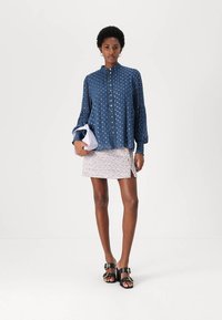 Kék gombos ing, fehér pöttyökkel, hosszú ujjú; egy texturált, mintás mini szoknyával párosítva. A modellen fekete szandál van.