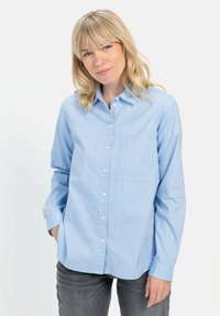 Lichtblauw overhemd met knoopsluiting in een zachte stof, met een voorzak en lange mouwen, gedragen met grijze broek.