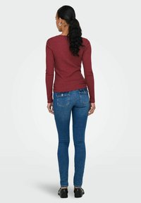 Langermet burgunder ribbet topp paret med blå skinny jeans. Antrekket har en tettsittende design med en glatt tekstur og subtile sømdetaljer.
