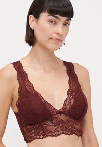 Burgundy lace bralette with a plunging neckline, scalloped edges, and floral patterns. Soft and sheer texture, featuring wide lace straps.