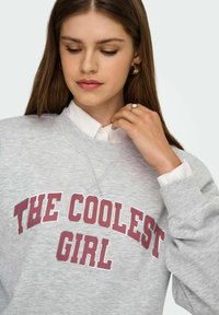 Hall triiksärk burgundia värvi trükitud tekstiga "THE COOLEST GIRL." Omadused: soonikkoes kaelus ja mansetid, pikad varrukad ning lõõgastunud sobivus.