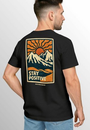 Black cotton t-shirt featuring a colorful graphic of mountains and a sun. The text "STAY POSITIVE" is prominently displayed.