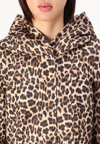 Leopard print hooded jacket featuring a textured fabric, with a mix of light beige, dark brown, and black spots. Zipper closure at front.