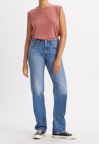 Top sin mangas de color rojo jaspeado con escote redondo, combinado con jeans rectos de color azul claro con un lavado desgastado y zapatillas negras clásicas.