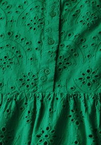 Abito in cotone verde con motivi floreali ricamati, dotato di bottoni arrotondati e orlo arricciato. Superficie testurizzata con dettagli intagliati.