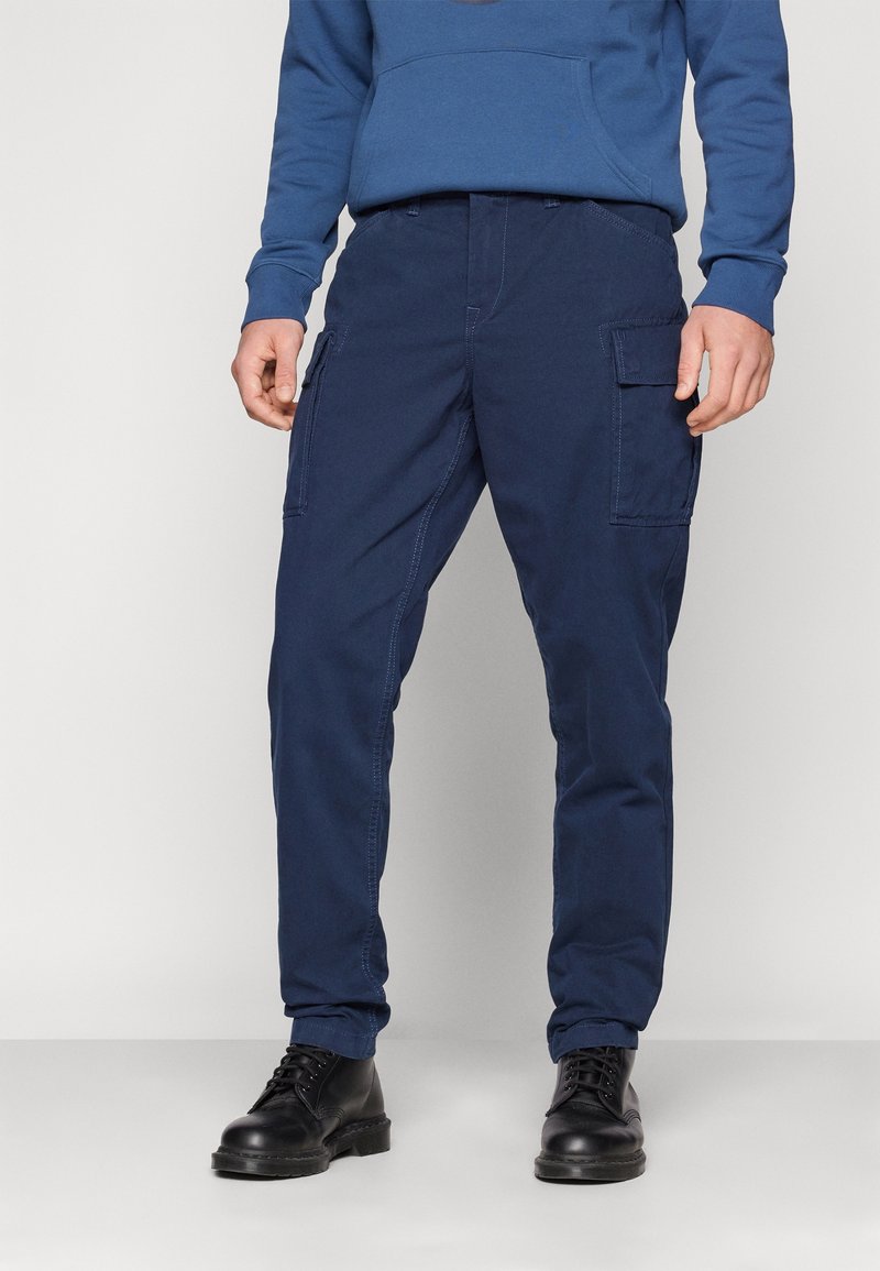 Pantalon cargo bleu marine en tissu mélange de coton, avec poches latérales, jambes droites et détail de couture visible.