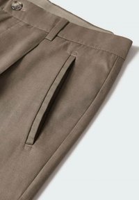 Pantalon beige en tissu léger, avec deux poches avant, une texture lisse et une ceinture plate avec une fermeture par bouton.