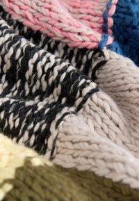 Knit blanket featuring thick yarn in black, white, pink, blue, and green sections, with a textured, multi-colored pattern.