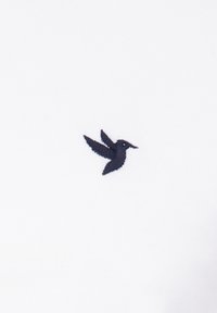 Tela blanca con un pequeño y detallado pájaro bordado en azul marino, con las alas extendidas, situado hacia la izquierda.