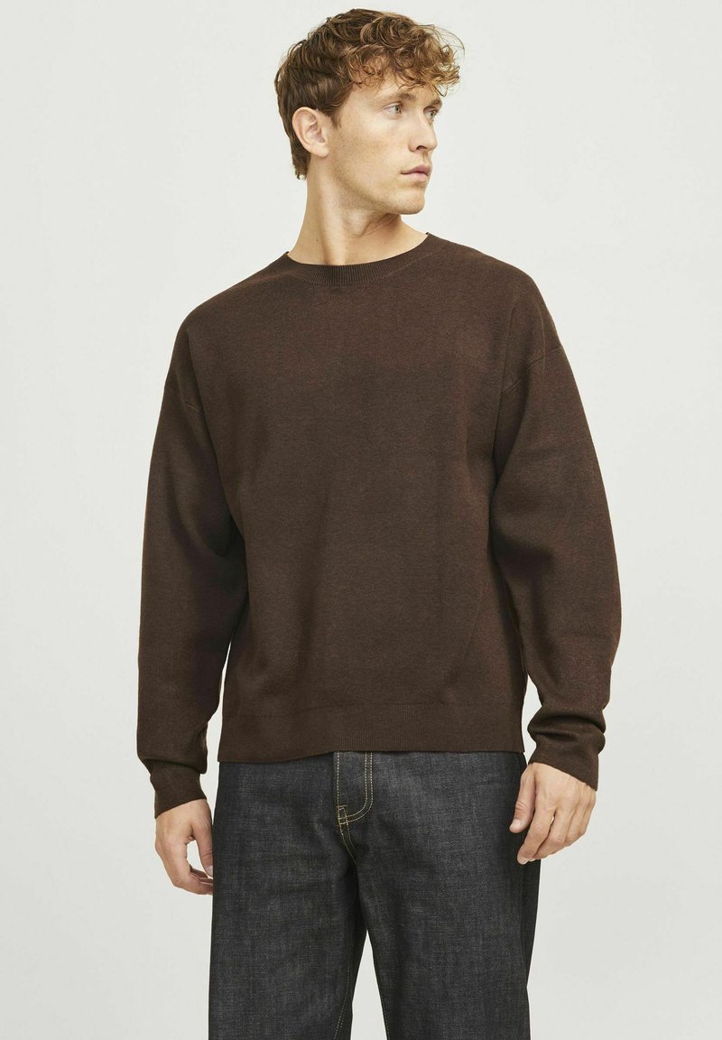 Maglione marrone con scollatura rotonda, spalle basse e maniche lunghe. Tessuto morbido e vestibilità rilassata, abbinato a jeans in denim scuro.
