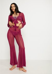 Conjunto de dos piezas de magenta transparente que incluye un top corto con lazo en la parte delantera y mangas largas, y pantalones acampanados con una textura estampada.