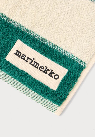 Близък план на кремава и зелена кърпа с пришит етикет, на който пише „marimekko“ с малки черни букви върху кремаво парче плат.