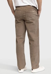 Brown corduroy pants with a relaxed fit, elastic waistband, and a back pocket, paired with white sneakers on a neutral background.