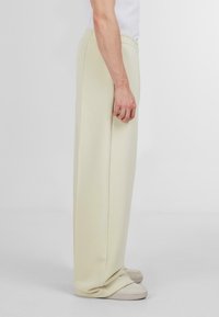 Pantaloni de trening bej deschis, cu o croială lejeră, talie elastică și detalii pe cusăturile laterale, asociați cu pantofi slip-on bej.