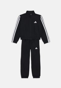 Tuta nera realizzata in tessuto liscio, con strisce bianche lungo le maniche e le gambe, giacca con zip e pantaloni con cintura elastica.