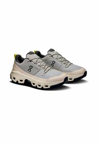 Hellgraue Sportschuhe aus Mesh-Obermaterial mit schwarzen Akzenten und gelbem Fersenloop. Gepolsterte Sohle mit ausgeschnittenem Design für Flexibilität.