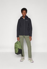 Veste zippée noire avec capuche, pantalon vert et sac à dos vert. Baskets avec des accents gris clair et violet. Texture lisse et design fonctionnel.