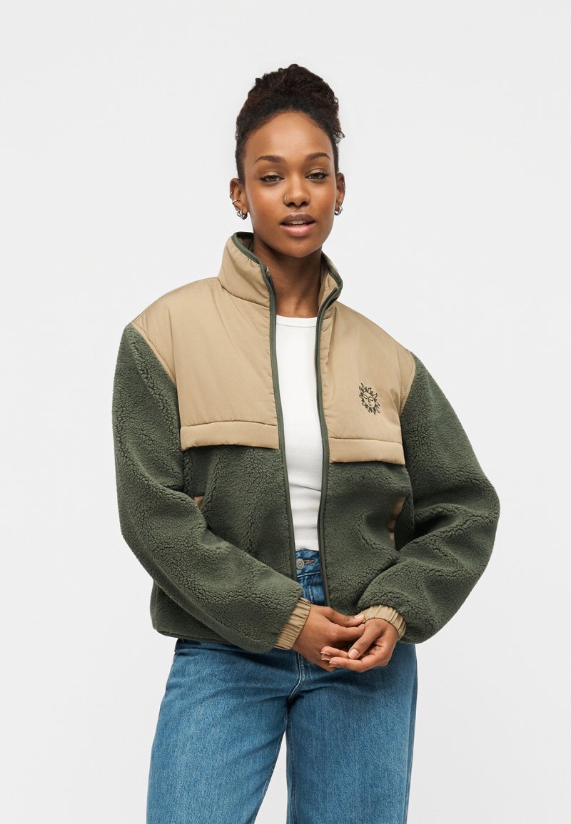 Ζακέτα από φλις με πράσινο κορμό, ταμπά επάνω πάνελ, ψηλό γιακά και κεντημένο λογότυπο. Περιλαμβάνει κλείσιμο με φερμουάρ και ριμπ μανσέτες.