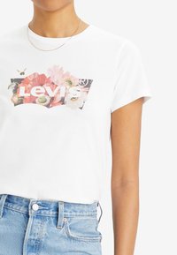 Vit bomull T-shirt med ett blommigt grafiktryck och "Levi's" text i fet stil. Korta ärmar och en avslappnad passform. Jeansshorts synliga nedan.