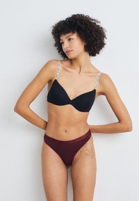 Black bra with adjustable straps featuring logo print; paired with maroon high-cut panties, smooth fabric and elastic waistband.
