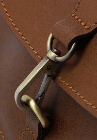 Dettaglio di una borsa in pelle marrone con cuciture in evidenza, una chiusura metallica in ottone e una texture liscia con finitura opaca.