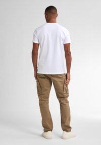 Camiseta blanca de manga corta combinada con pantalones cargo color caqui que cuentan con bolsillos laterales, un ajuste holgado, y zapatillas crema sobre un fondo neutro.