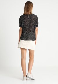 Černá blůzka s puntíky, krátkými puff rukávy, průhlednou tkaninou a detailem ve tvaru klíčové dírky na zadní straně. Kombinováno s lehkou béžovou denimovou minisukní.