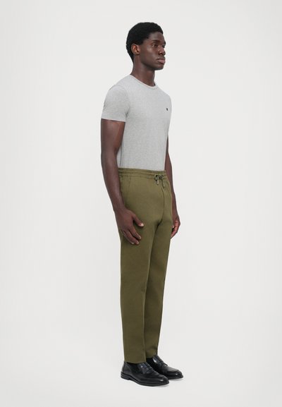 Grå t-shirt med korte ærmer, olivengrønne snørebukser og sorte sko. Glat tekstur, tætsiddende design og minimal branding på t-shirten.