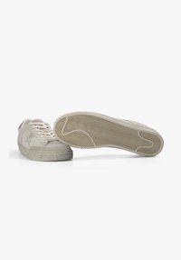 Par de zapatillas informales beige con cordones blancos, una mostrando la parte superior y lateral, la otra mostrando el patrón texturizado de la suela.