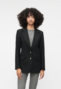 Mustat räätälöidyt bleiserit kultanappien kanssa, leikattu kaulus, kaksi etutaskua, päällä musta-valkoinen kuvioitu paita ja houndstooth-housut.