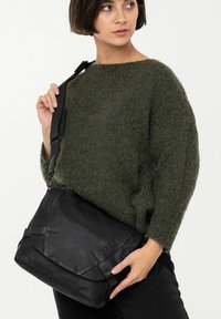 Borsa a tracolla in pelle nera con cinturino regolabile, caratterizzata da una superficie testurizzata e un design minimalista, accentuata da cuciture marrone scuro.