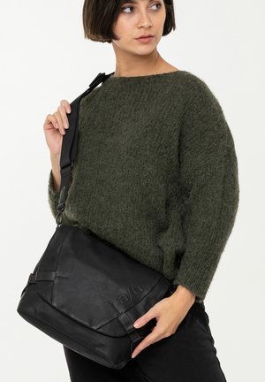 Borsa a tracolla in pelle nera con cinturino regolabile, caratterizzata da una superficie testurizzata e un design minimalista, accentuata da cuciture marrone scuro.
