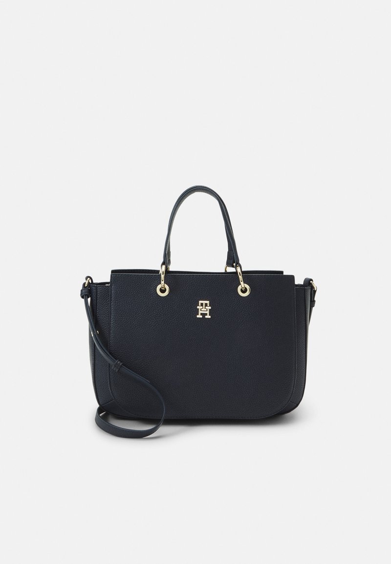 Sac à main en cuir noir avec deux poignées, bandoulière amovible, et logo ainsi que des accessoires en métal doré sur un fond uni.
