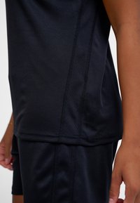 Czarna sportowa koszulka o gładkiej teksturze, z siateczkowym panelem wzdłuż bocznego szwu, uzupełniona pasującymi szortami.