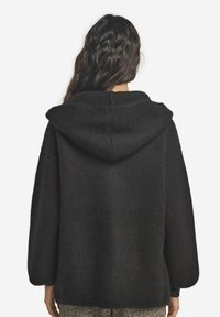 Svart huva tröja med en lös, oversized passform. Strukturerad stickad tyg, sänkt axlar och breda ärmar. Minimalistisk design utan utsmyckningar.