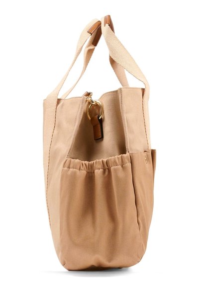 Beige canvas draagtas met brede schouderbanden, elastische zijzakken en een gouden metalen ringdetail vlak bij de bovenkant van de opening.